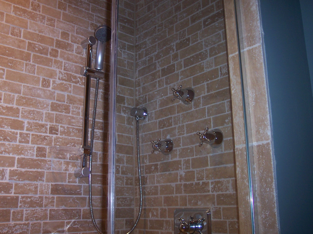 Stone-tile shower with chrome handheld showerhead and cross-handle controls
