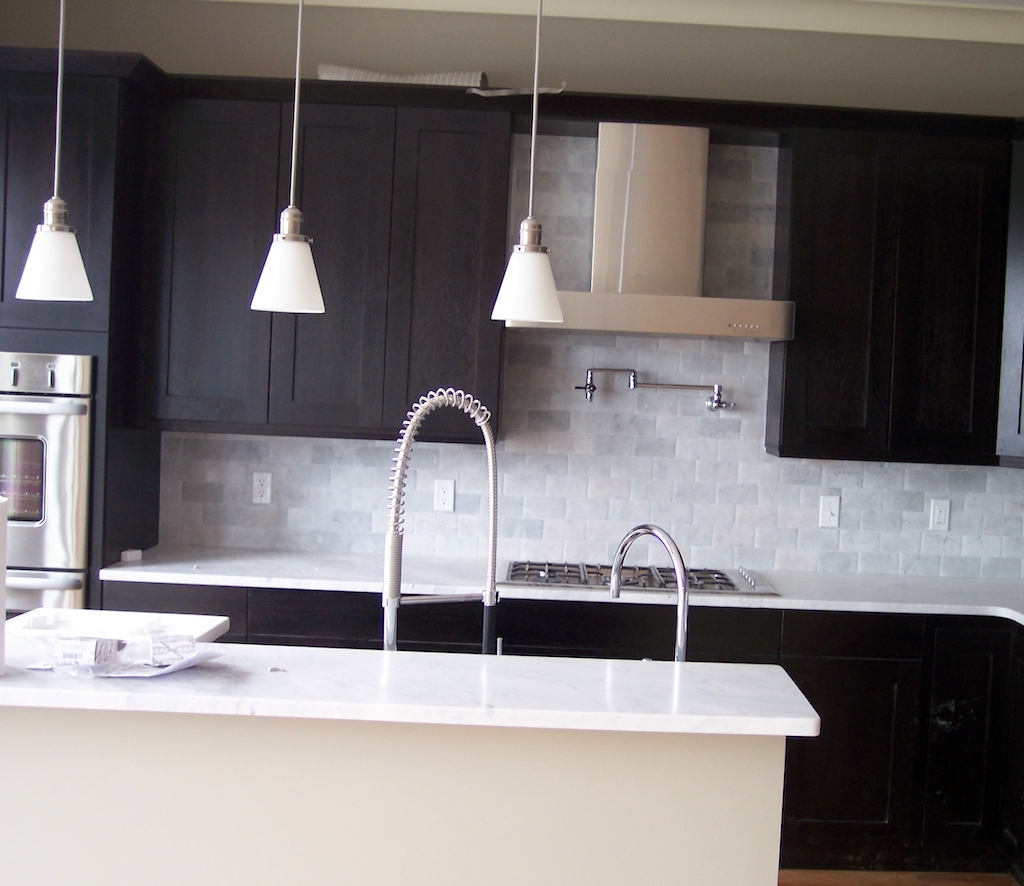 Dark cabinetry kitchen with marble countertops, pot filler, and pendant lighting