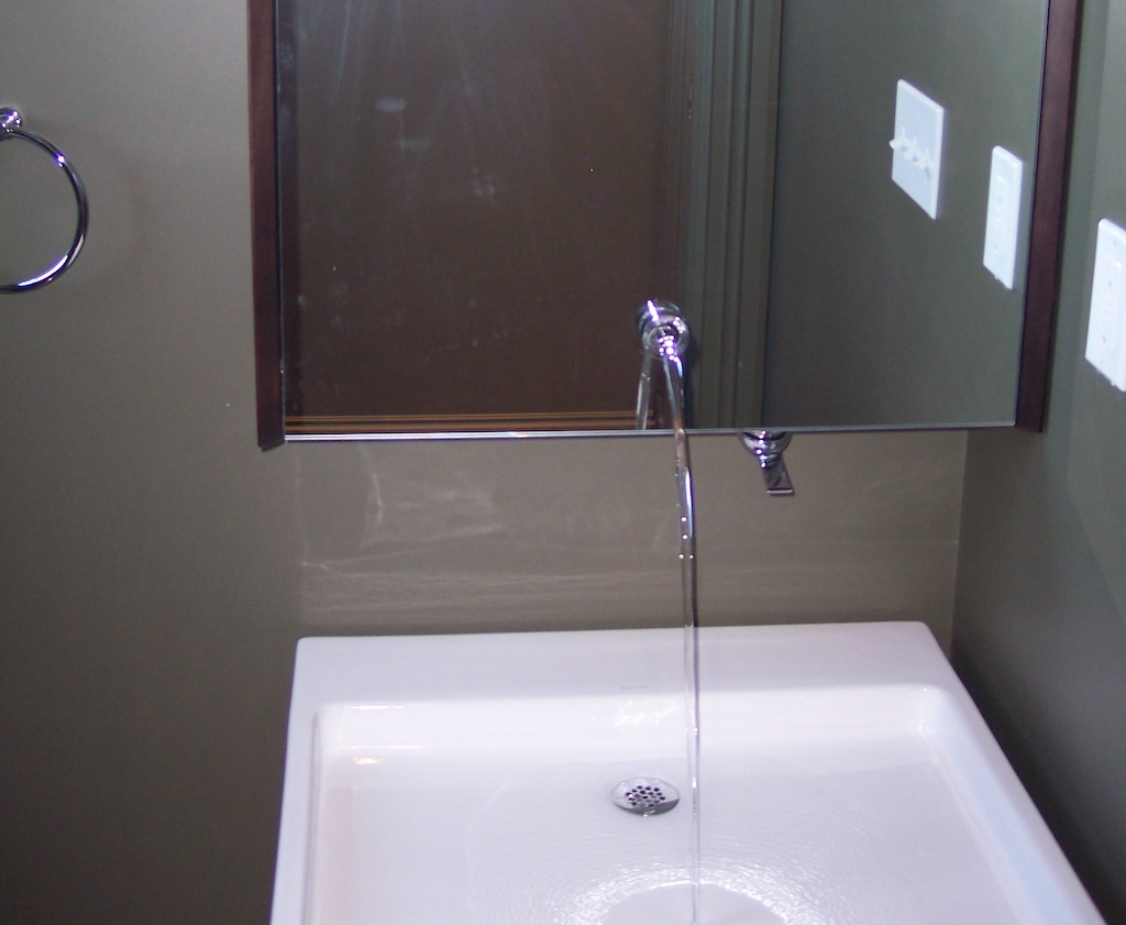 Wall-mounted chrome faucet with running water over a white rectangular sink