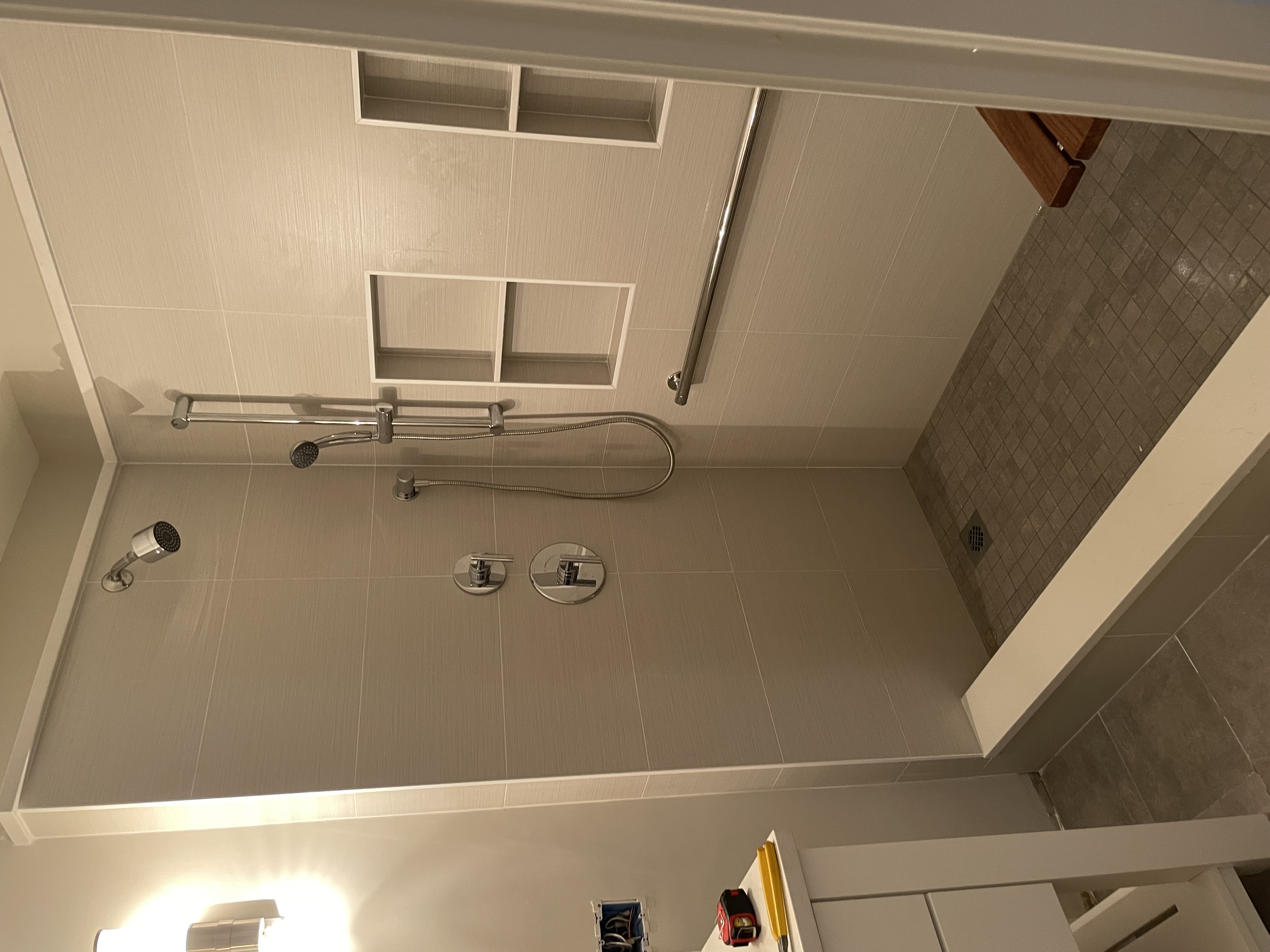 Walk-in shower with beige wall tile, mosaic floor, built-in niches, and grab bar
