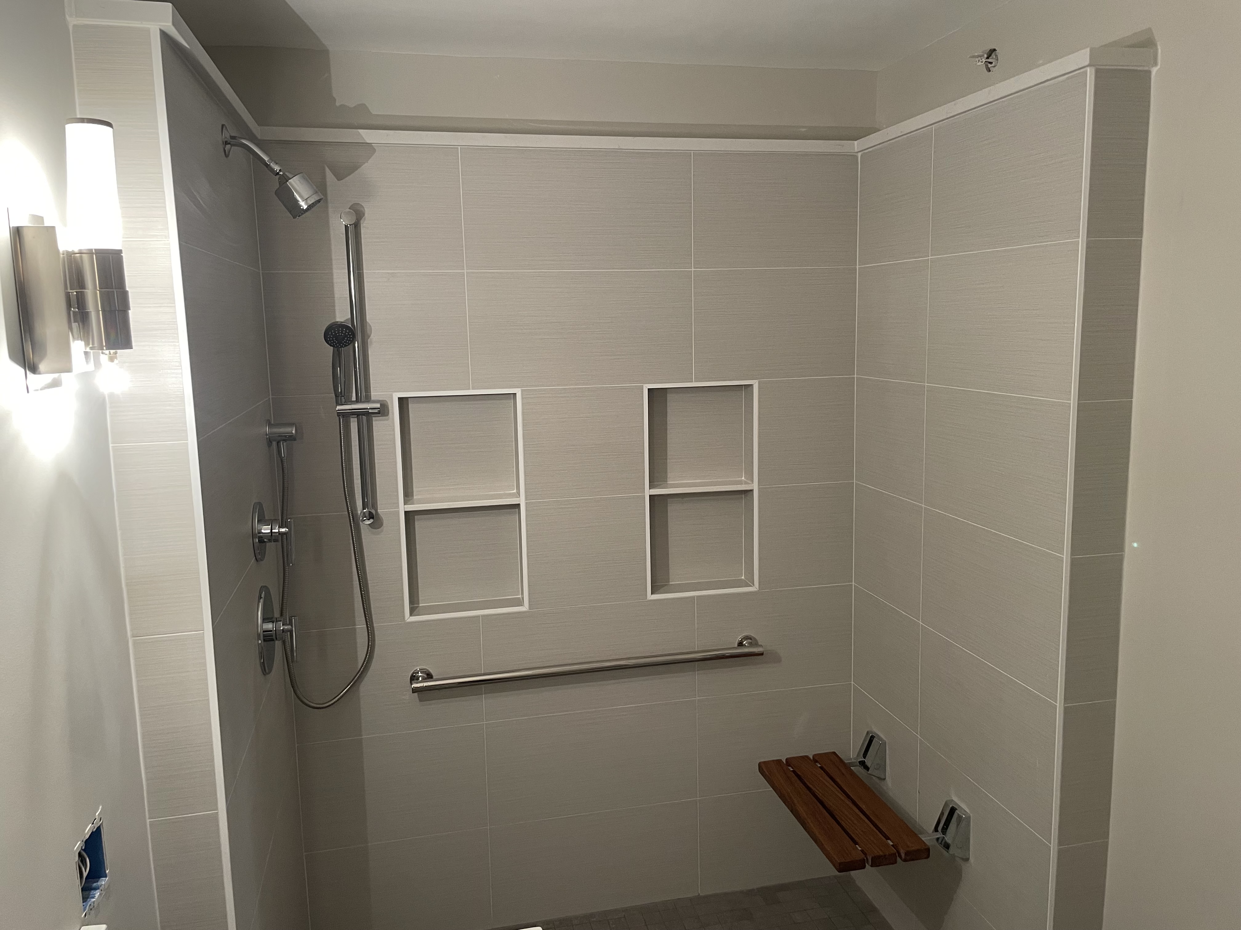 Accessible walk-in shower with fold-down bench, grab bar, and recessed storage niches