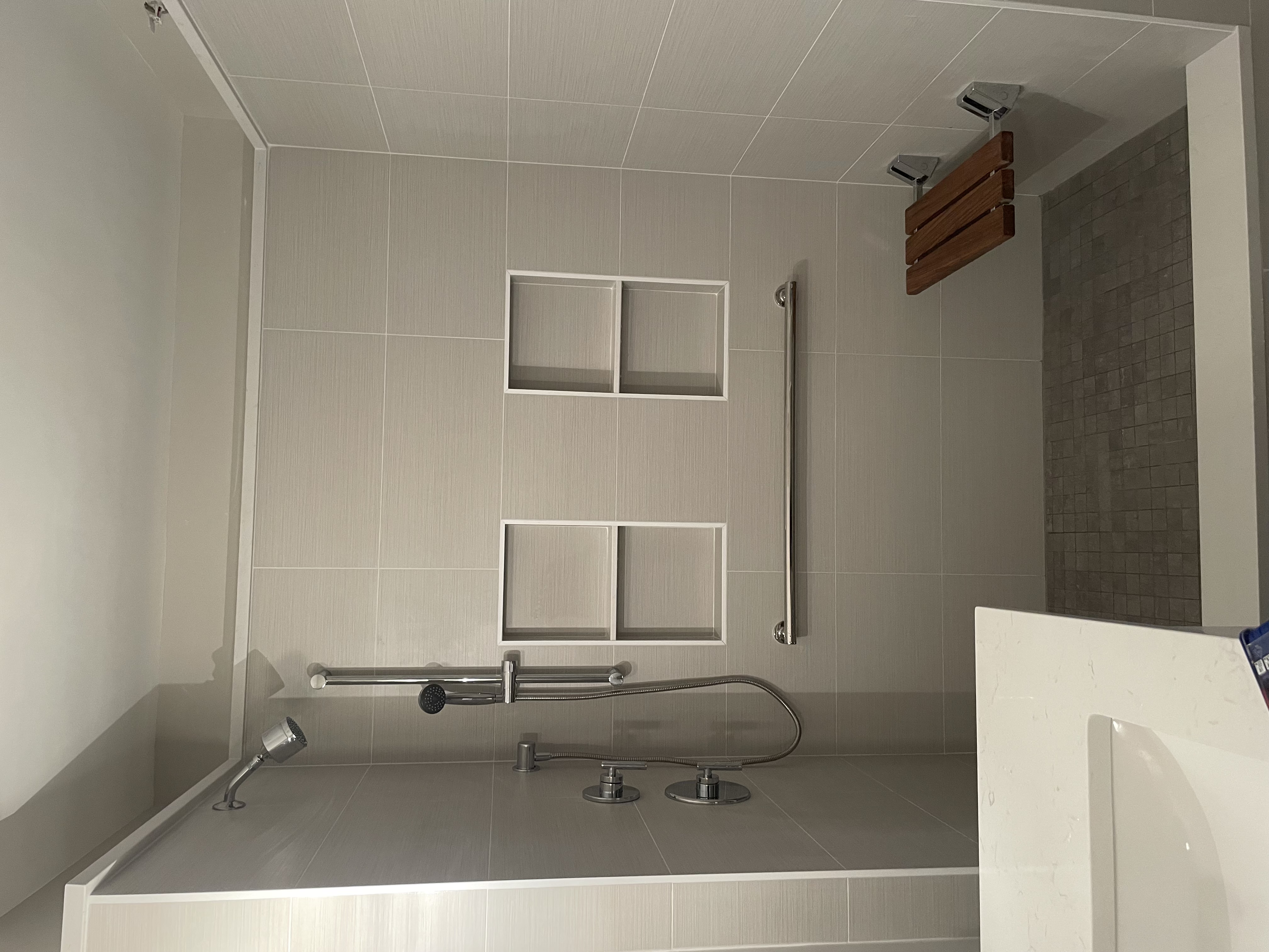 Modern walk-in shower with chrome fixtures, wall niches, and fold-down wooden bench