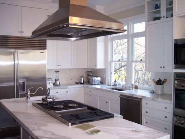 White kitchen with marble island, gas cooktop, and stainless steel appliances