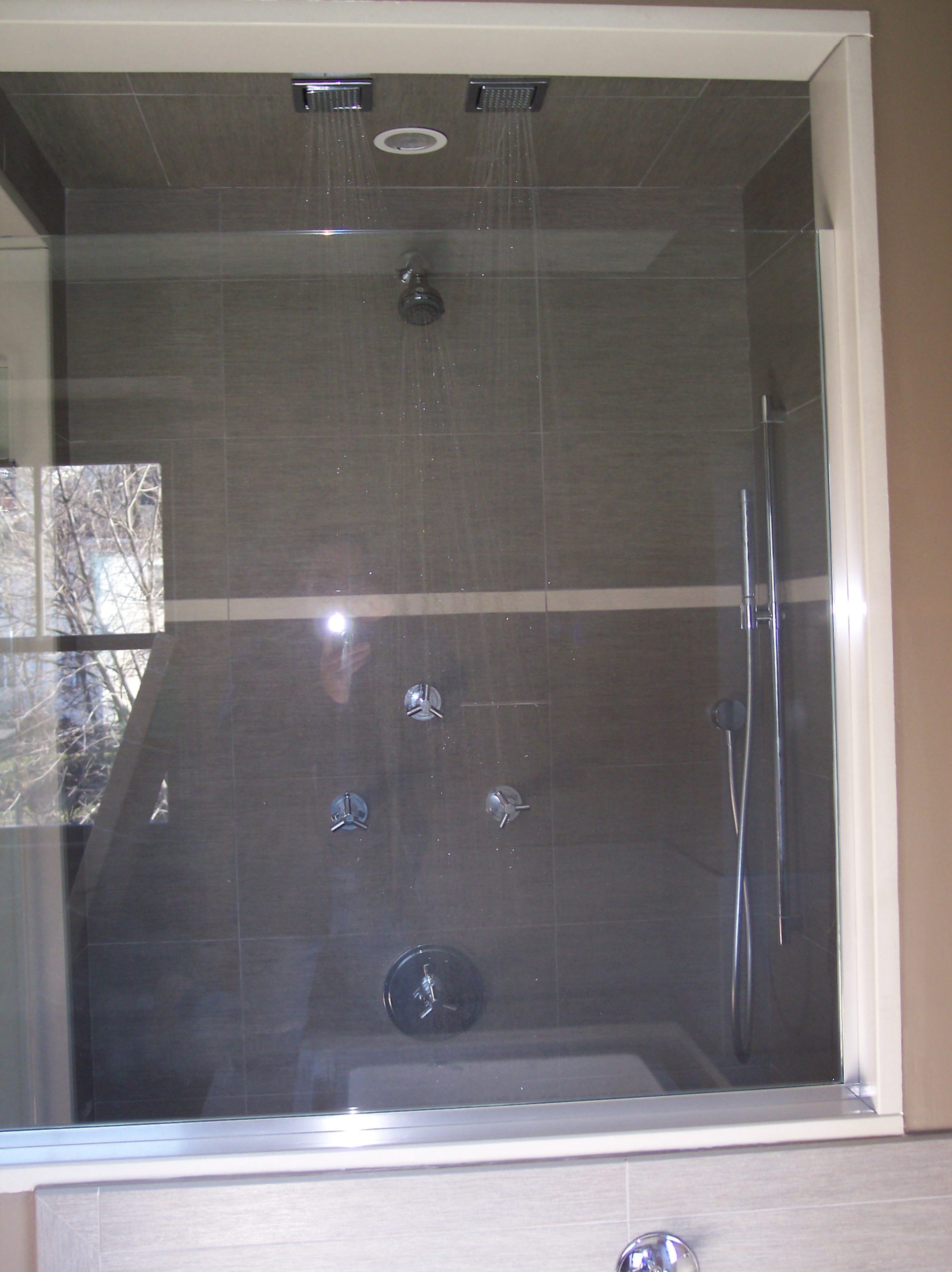 Glass-enclosed shower with dual rain heads, handheld wand, and dark tile walls
